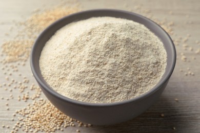 Photo of Ceramic bowl with quinoa flour and seeds on wooden table, closeup