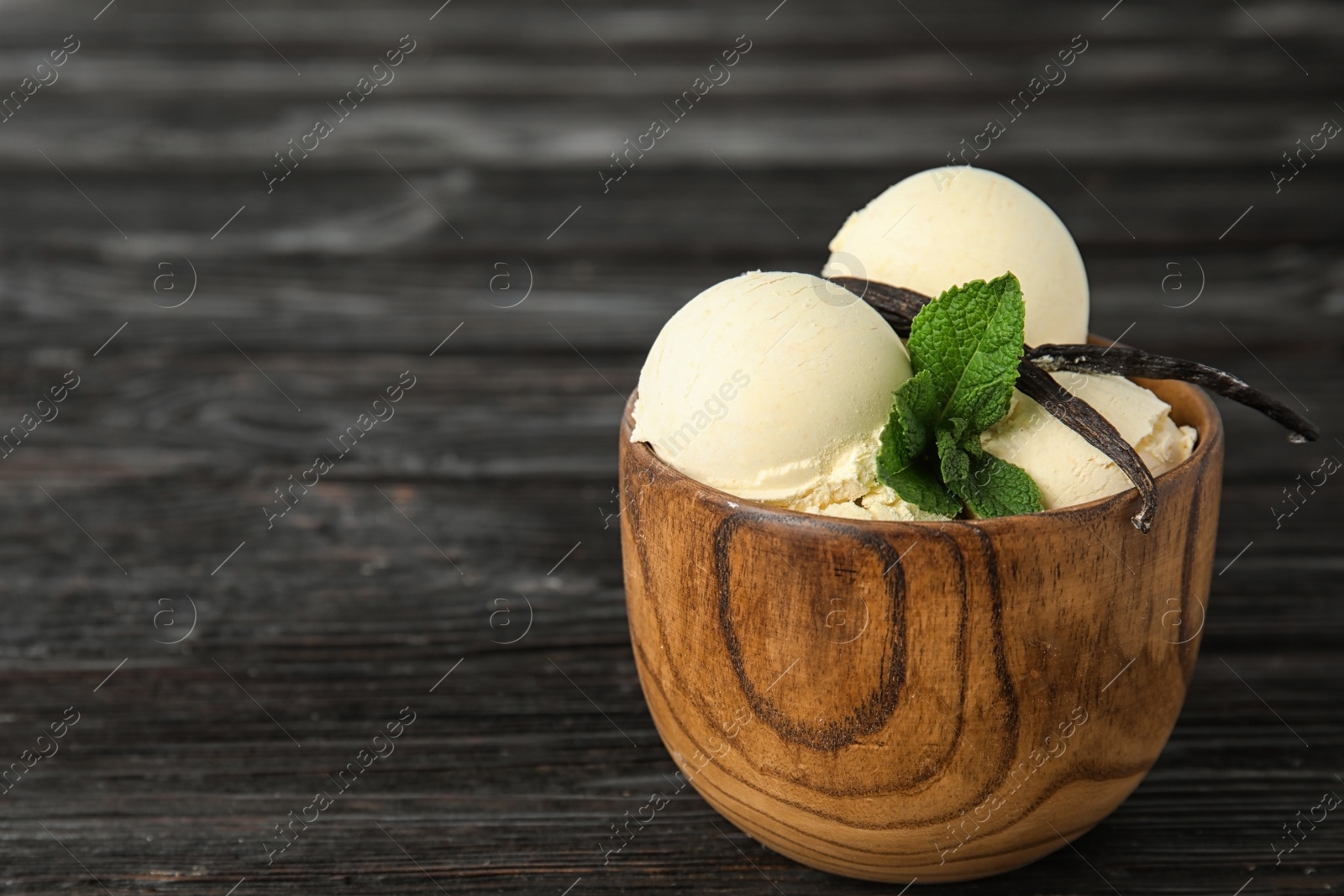 Photo of Delicious vanilla ice cream with mint and pods served on wooden table. Space for text