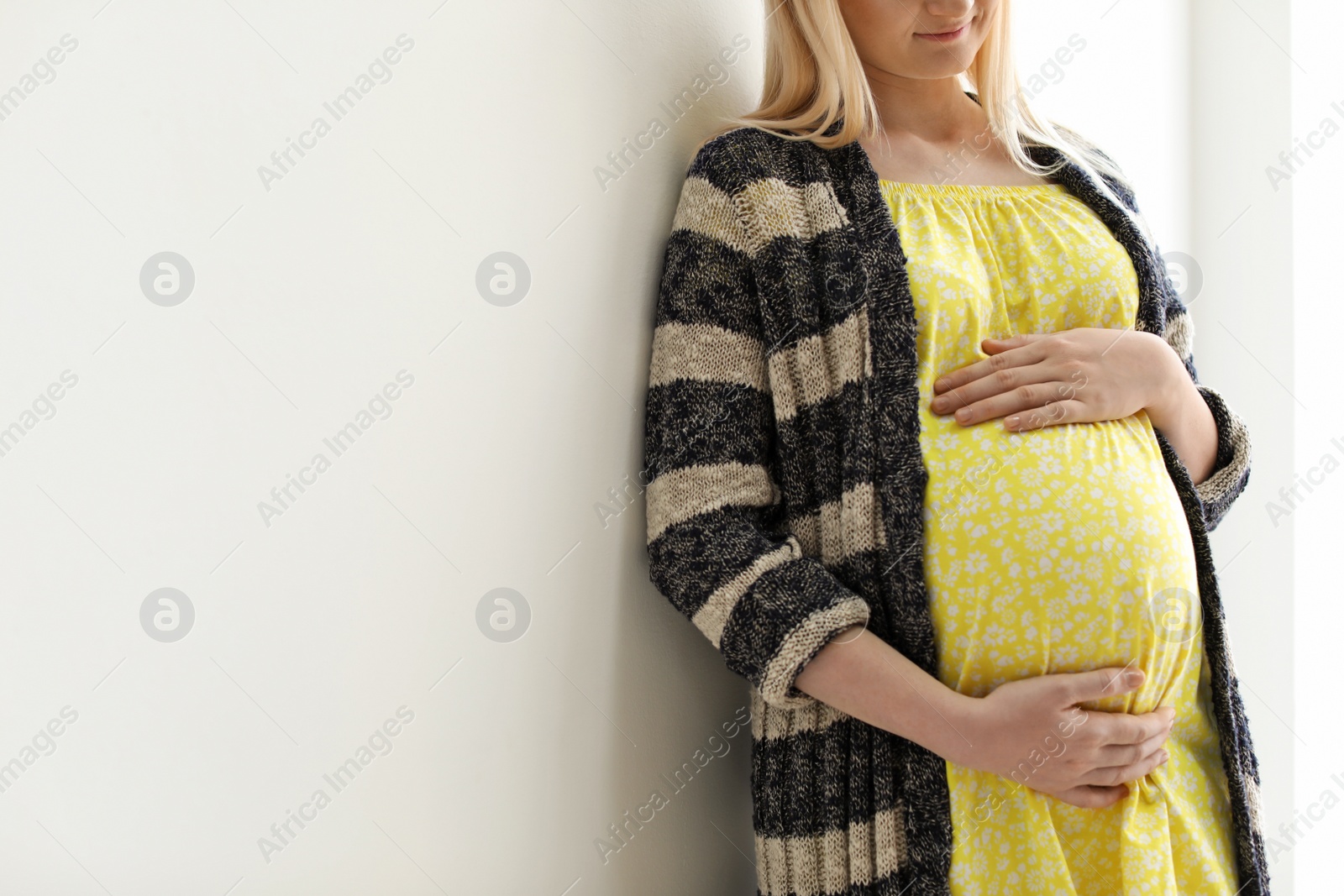 Photo of Pregnant woman near light wall. Space for text