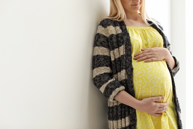 Pregnant woman near light wall. Space for text