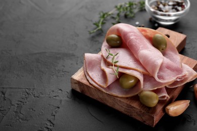 Photo of Tasty ham with olives, garlic and thyme on black textured table, closeup. Space for text