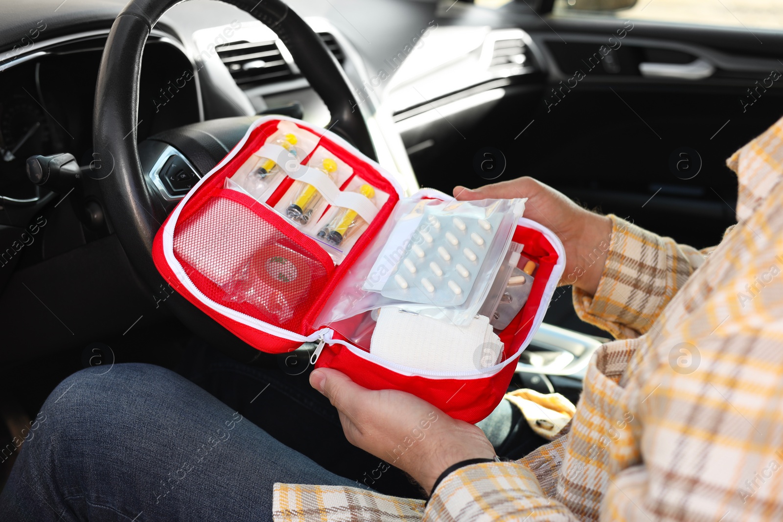 Photo of Man holding first aid kit with medicaments inside car, closeup