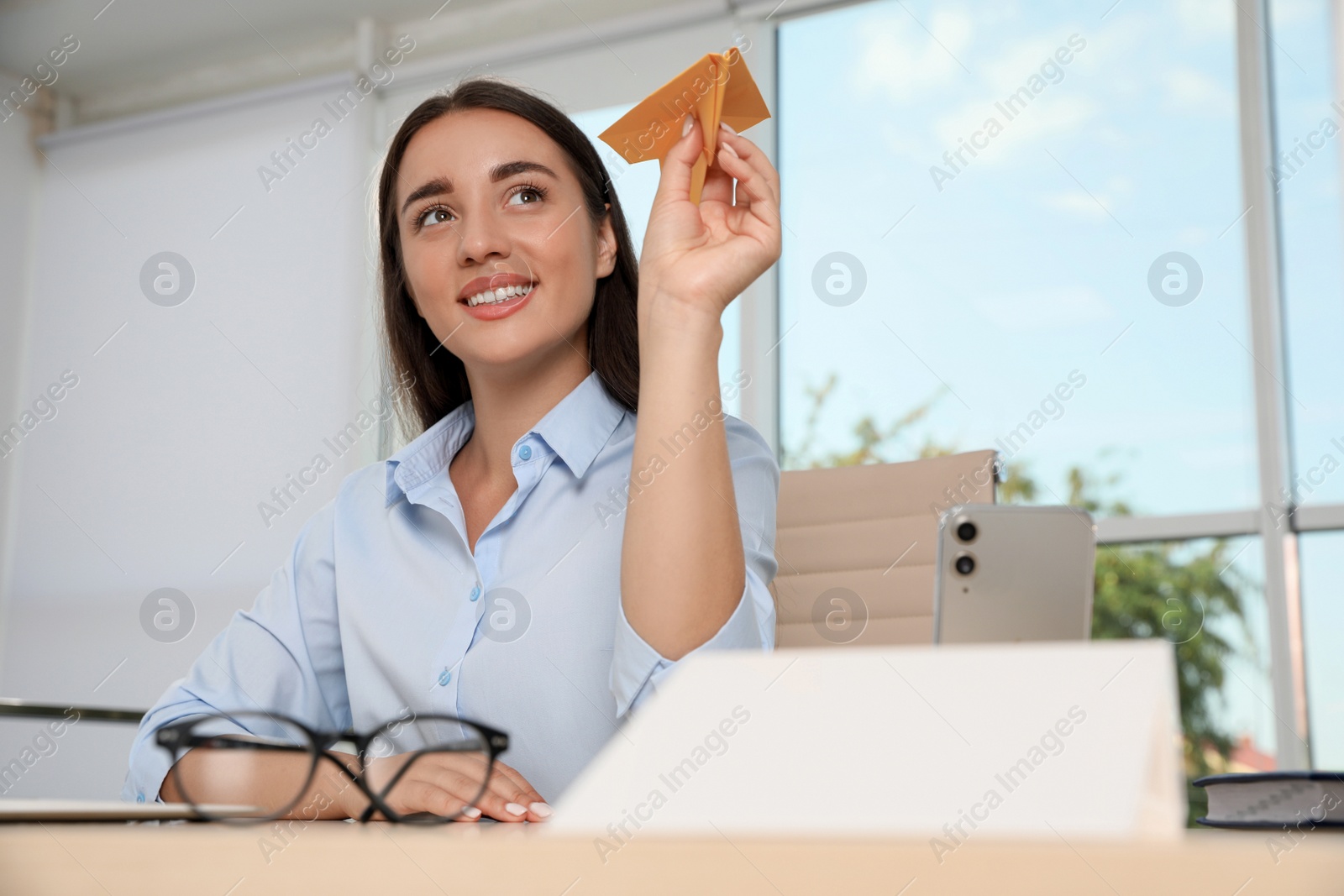 Photo of Beautiful young woman playing with paper plane at desk in office