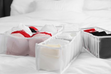 Photo of Organizers with stylish women's underwear on bed, closeup