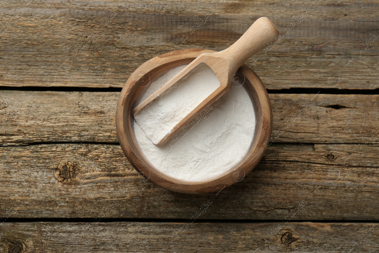 Photo of Baking powder in bowl and scoop on wooden table, top view