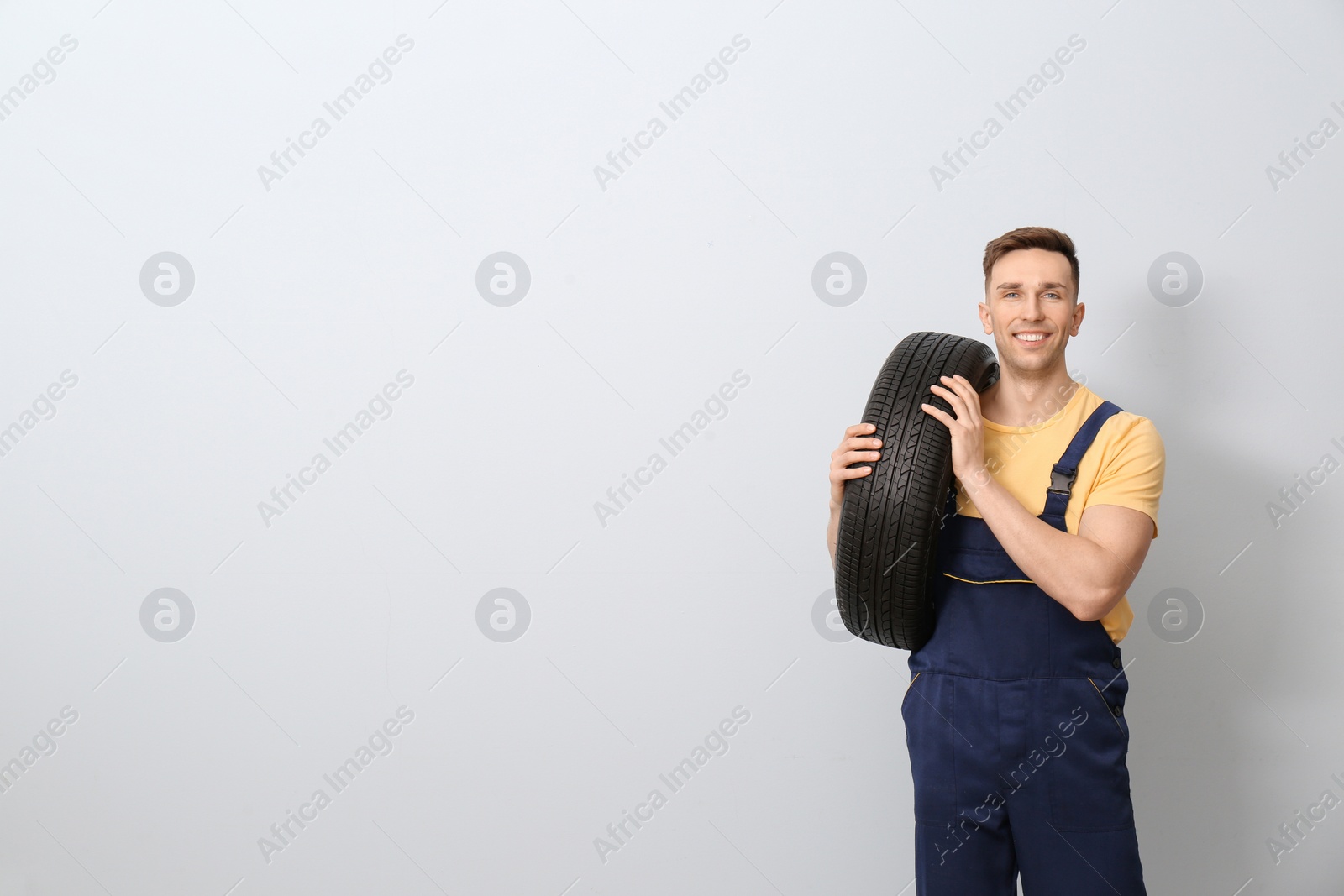 Photo of Male mechanic with car tire on light background