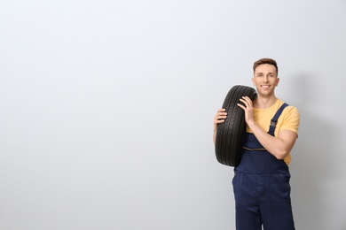 Photo of Male mechanic with car tire on light background