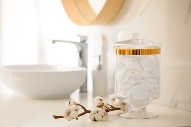 Photo of Jar with cotton pads and flowers on countertop in bathroom