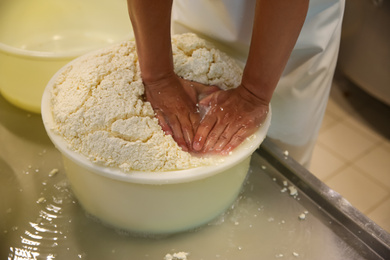 Photo of Worker pressing curd into mould at cheese factory, closeup