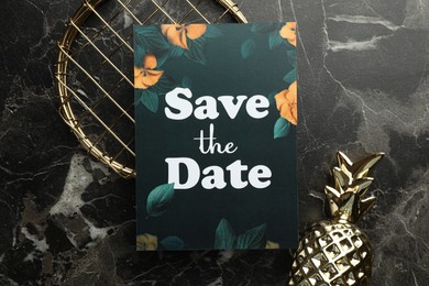 Photo of Beautiful card with Save the Date phrase and decor elements on black marble background, flat lay