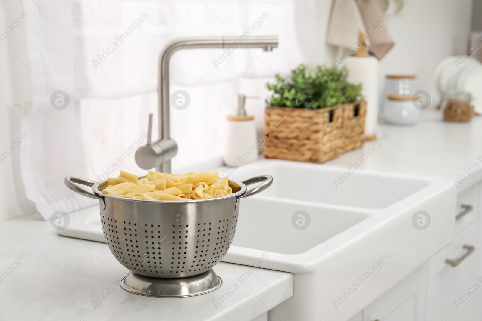 Photo of Cooked pasta in metal colander on countertop near sink. Space for text