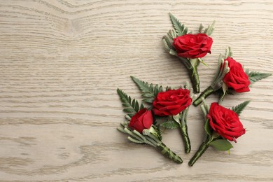 Photo of Many stylish red boutonnieres on light wooden table, flat lay. Space for text