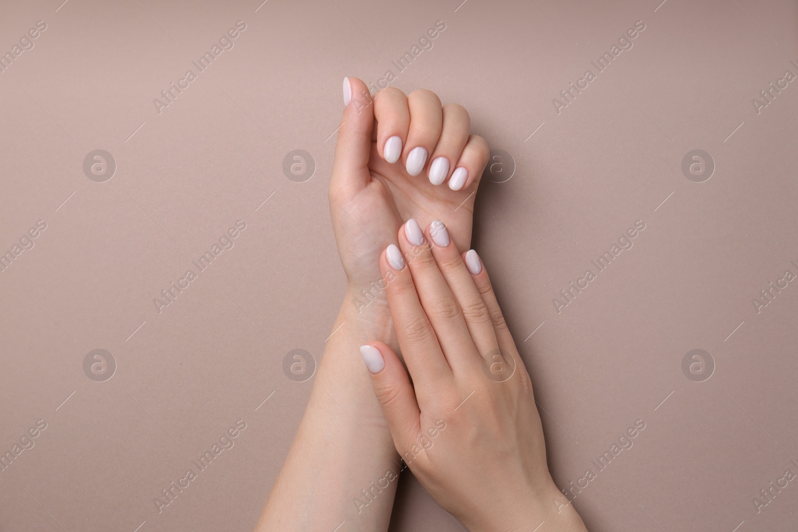 Photo of Woman showing her manicured hands with white nail polish on light brown background, top view