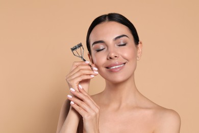 Photo of Beautiful young woman with eyelash curler on beige background