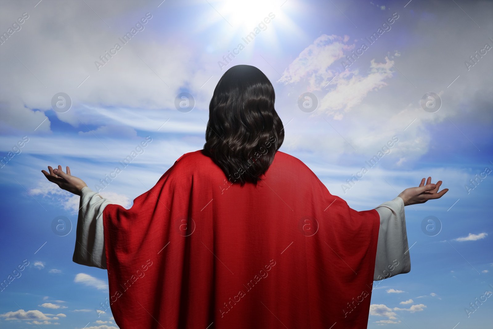 Image of Jesus Christ with outstretched arms against blue sky, back view