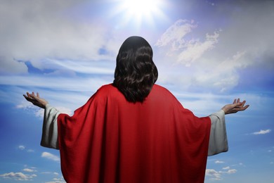 Image of Jesus Christ with outstretched arms against blue sky, back view