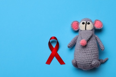 Photo of Cute knitted toy mouse and red ribbon on blue background, flat lay with space for text. AIDS disease awareness