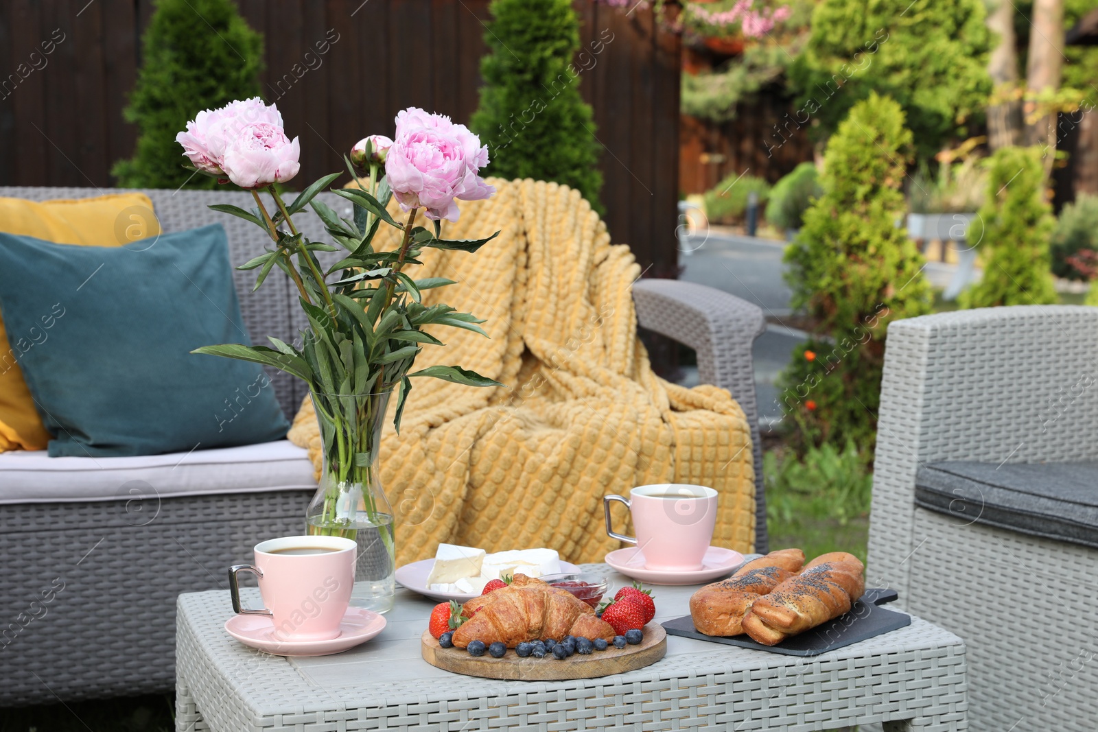 Photo of Morning drink, pastry, berries, cheese and vase with flowers on rattan table. Summer breakfast outdoors