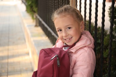 Photo of Cute little girl with backpack on city street. Space for text