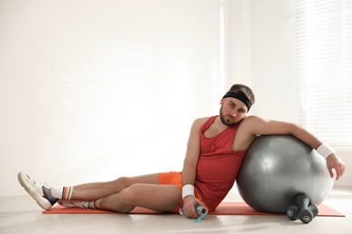 Photo of Lazy young man with sport equipment on yoga mat indoors. Space for text