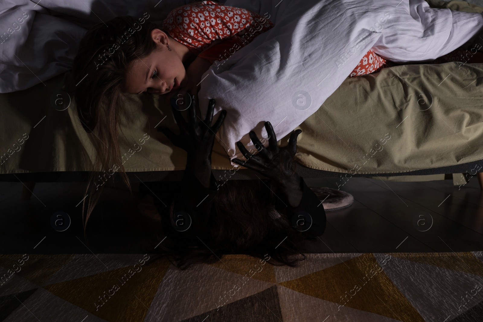 Photo of Childhood phobia. Little girl looking at monster under bed indoors