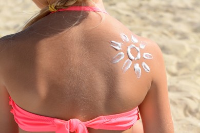 Photo of Little girl with sun protection cream on body outdoors, closeup