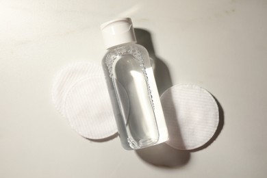 Photo of Bottle of micellar cleansing water and cotton pads on white table, flat lay