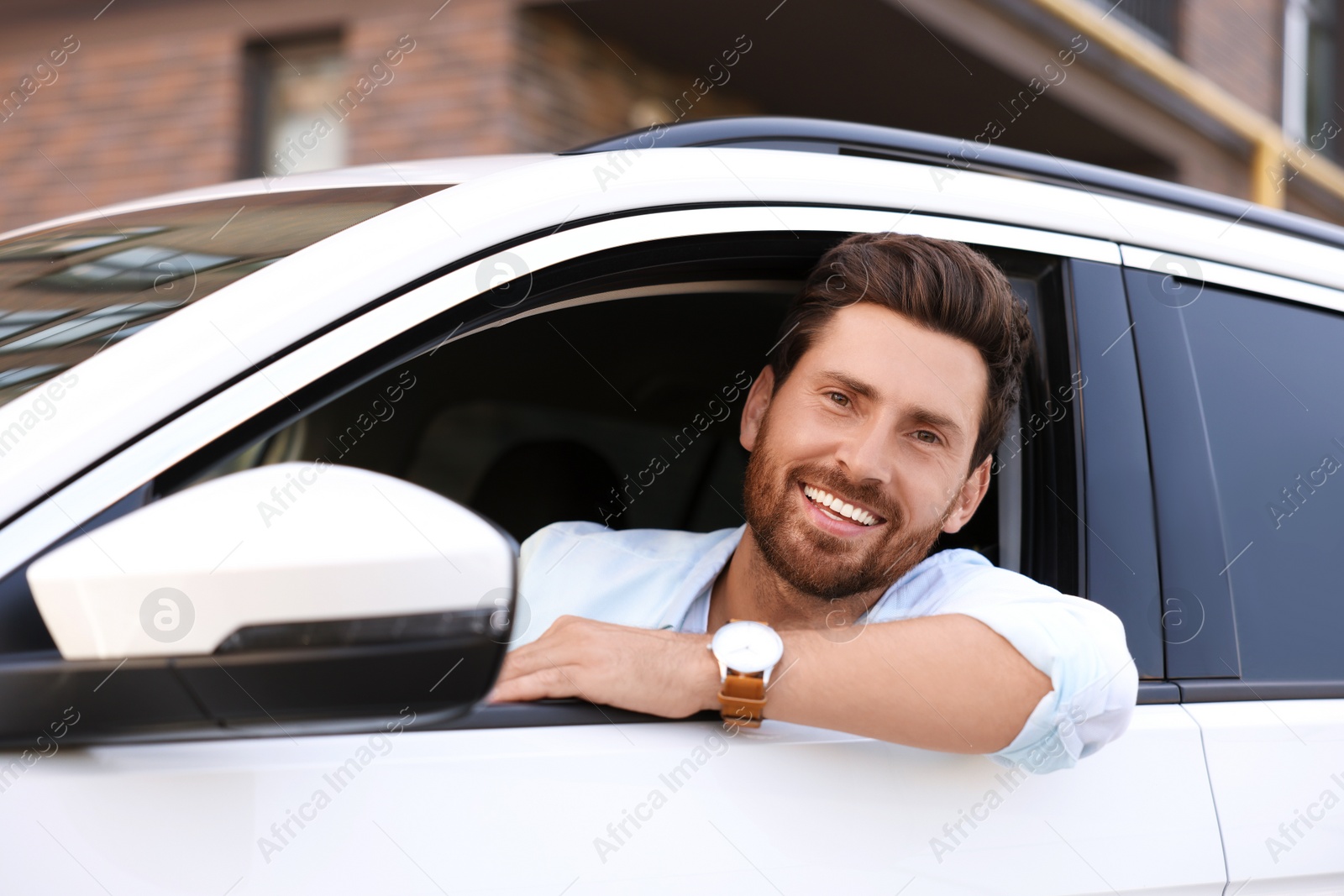 Photo of Happy bearded man looking out of car window on city street, view from outside. Enjoying trip