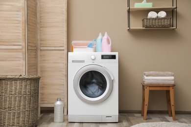 Photo of Modern washing machine near color wall in laundry room interior