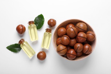 Photo of Delicious organic Macadamia nuts, green leaves and natural oil on white background, flat lay