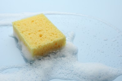 Yellow sponge with foam on light blue background, closeup