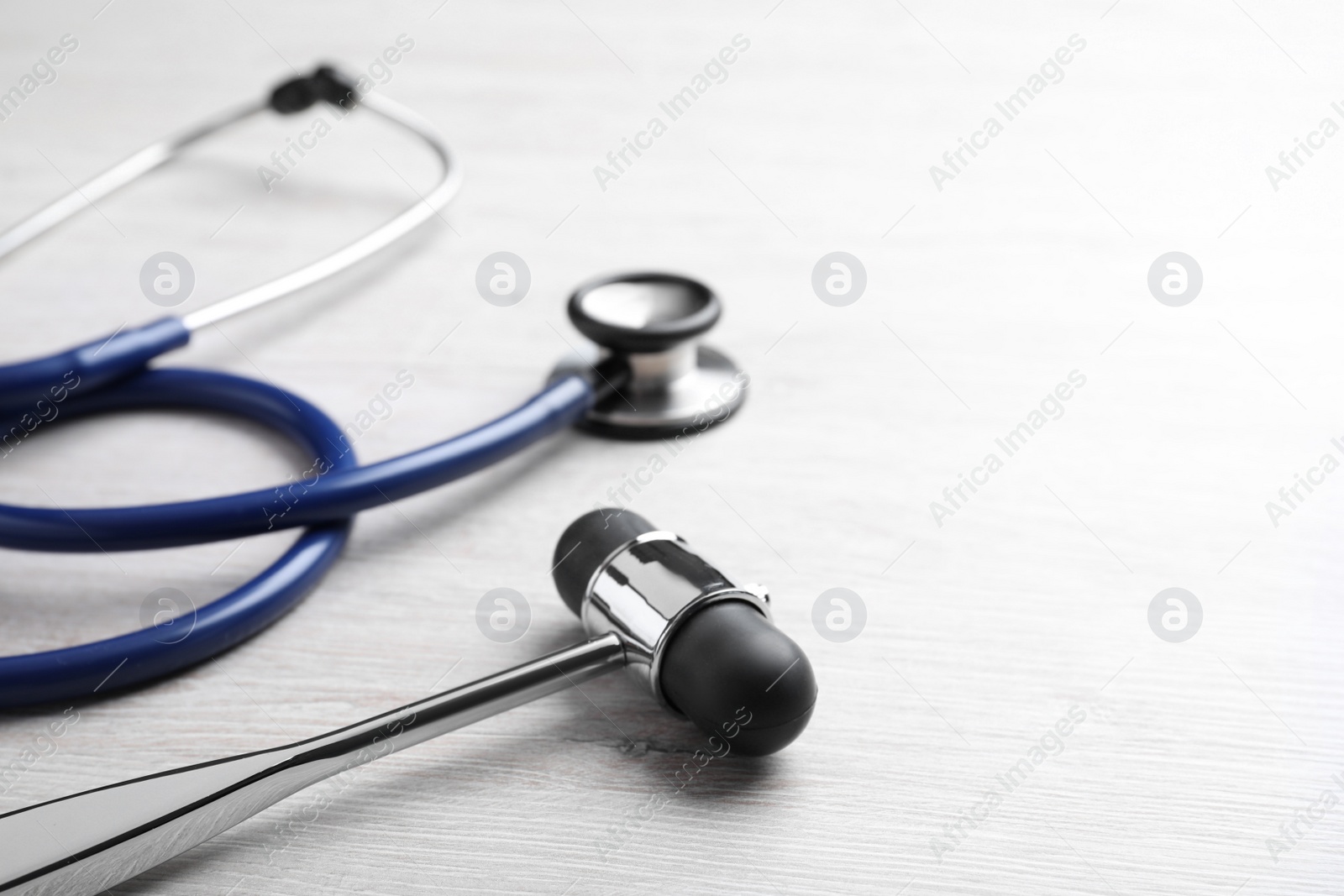 Photo of Reflex hammer with stethoscope on light wooden background, closeup. Nervous system diagnostic
