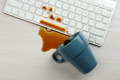 Cup of coffee spilled over computer keyboard on white wooden table, flat lay