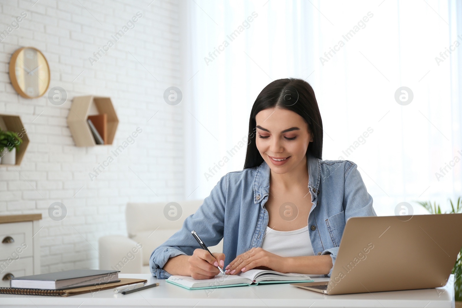 Photo of Young woman taking notes during online webinar at table indoors