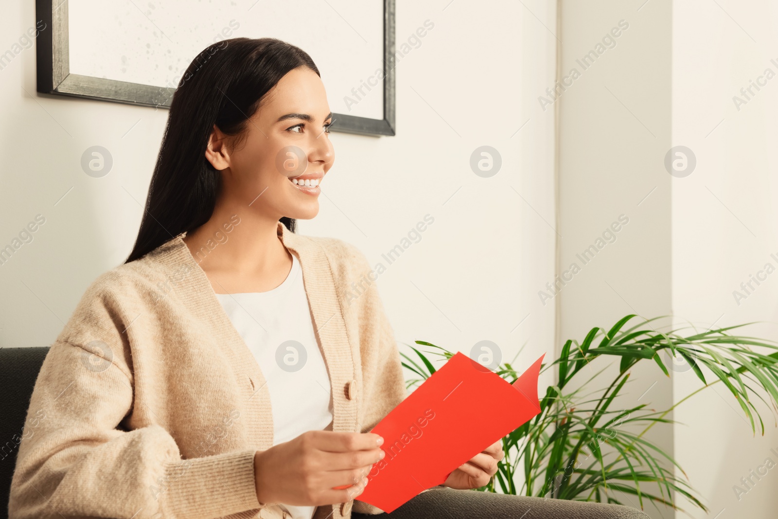 Photo of Happy woman reading greeting card on sofa in living room