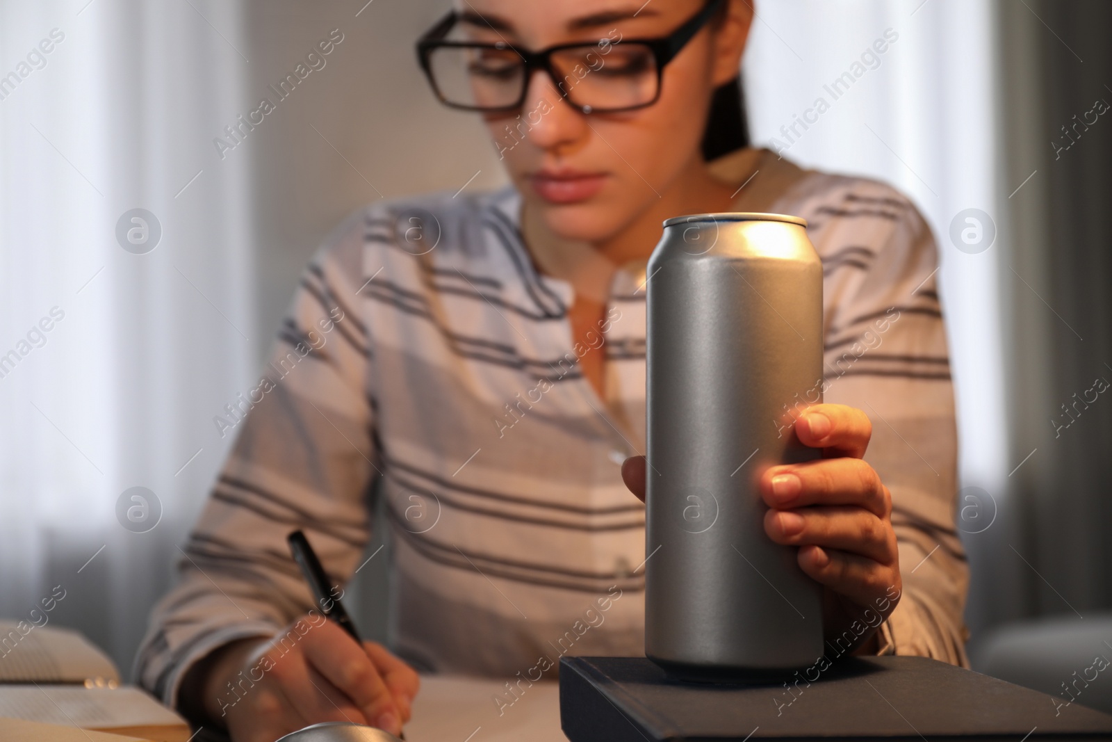 Photo of Tired young woman with energy drink studying at home, focus on hand