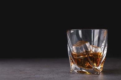 Photo of Golden whiskey in glass with ice cubes on table. Space for text