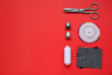 Flat lay composition with thimbles and different sewing tools on red background. Space for text