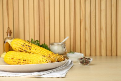 Photo of Plate with tasty grilled corn on wooden table. Space for text