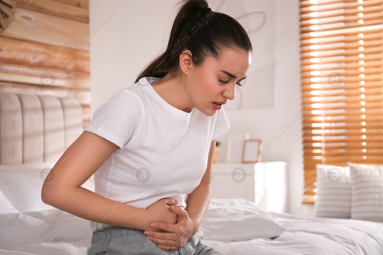 Photo of Young woman suffering from stomach ache on bed at home. Food poisoning