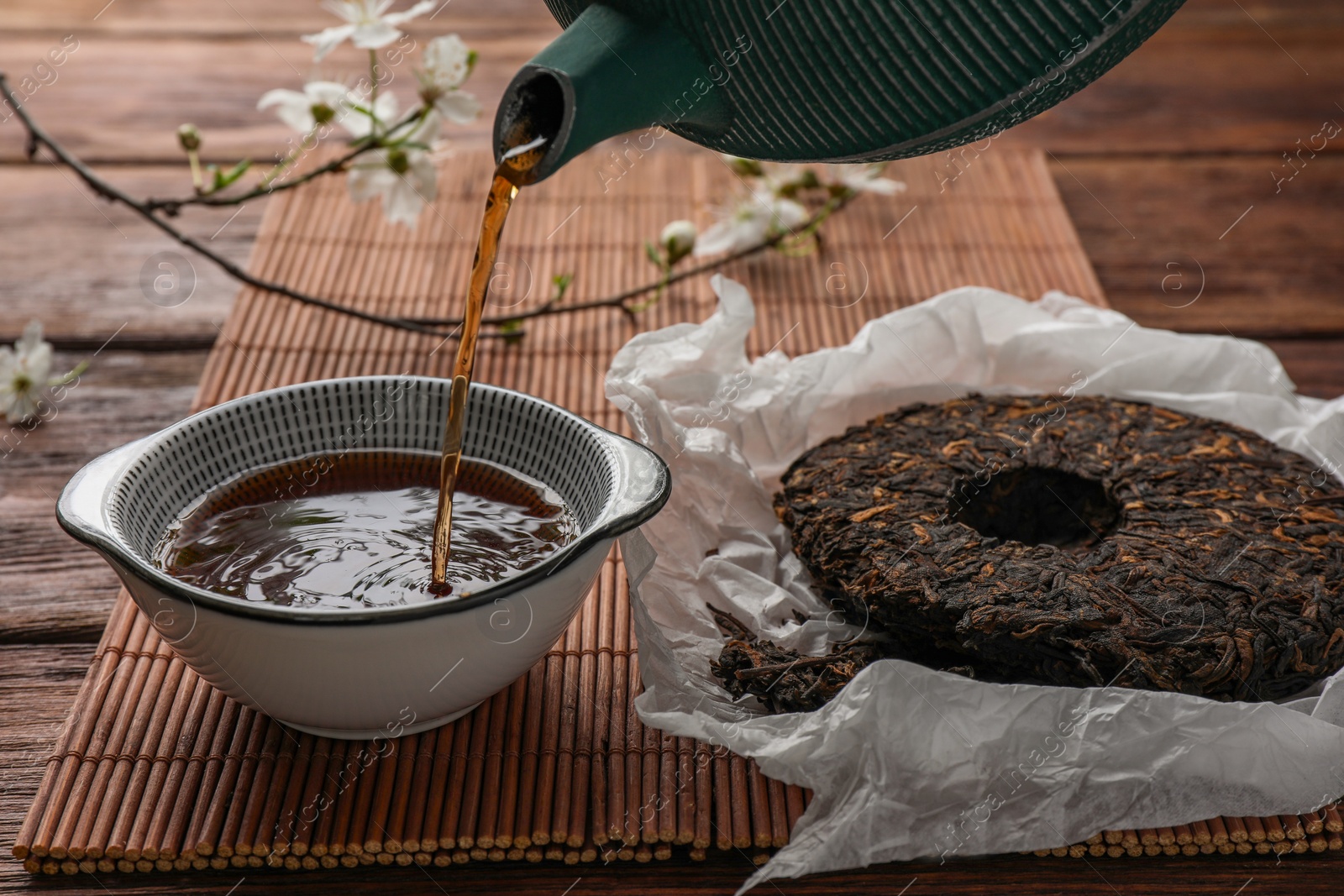 Photo of Pouring freshly brewed pu-erh tea into cup on wooden table, closeup