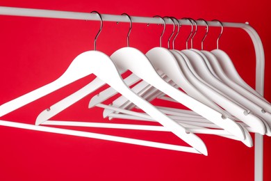 Photo of White clothes hangers on metal rack against red background, closeup