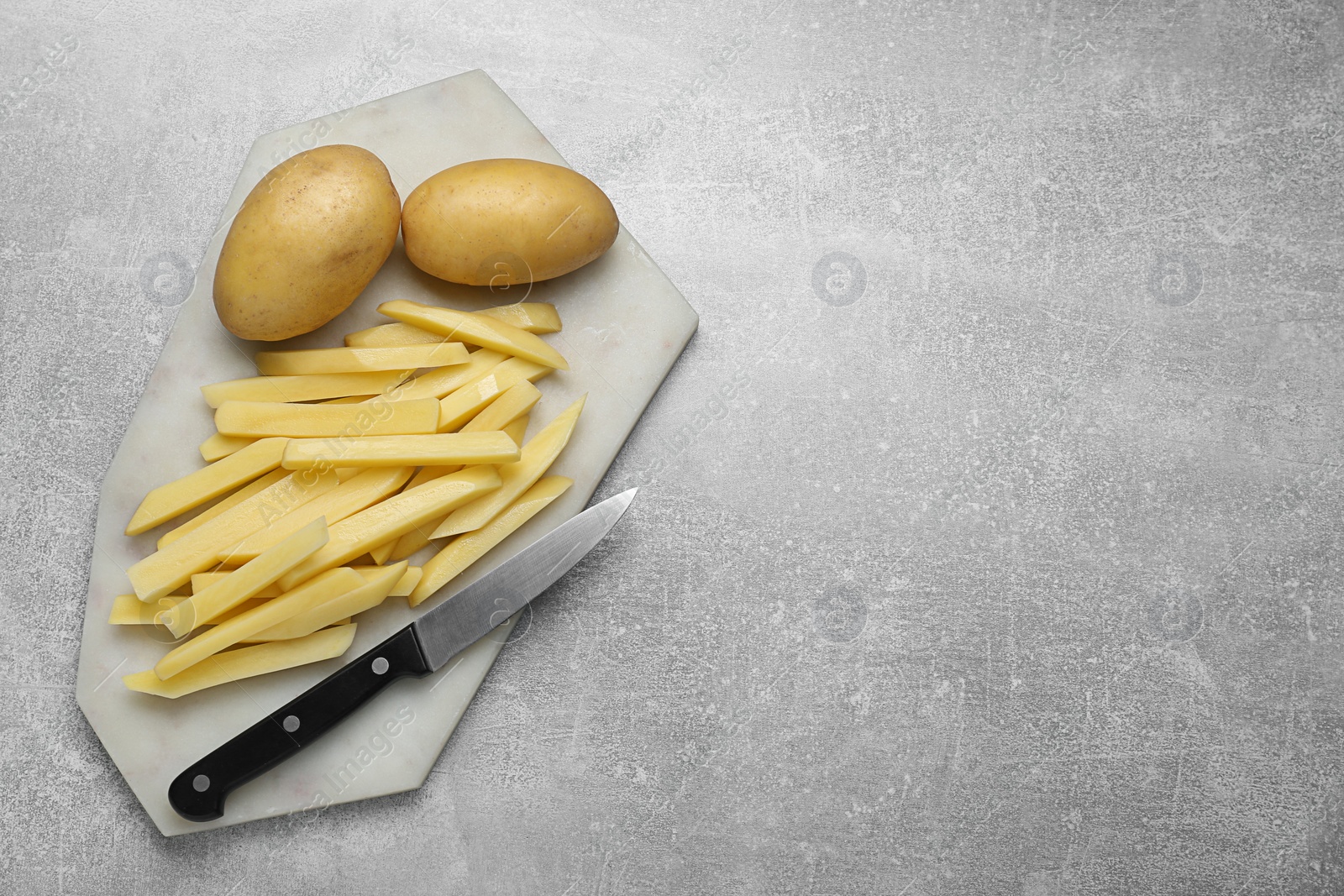 Photo of Whole and cut raw potatoes with knife on light grey table, top view. Space for text. Cooking delicious French fries