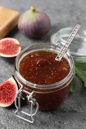 Jar of tasty sweet jam and fresh figs on grey table, closeup