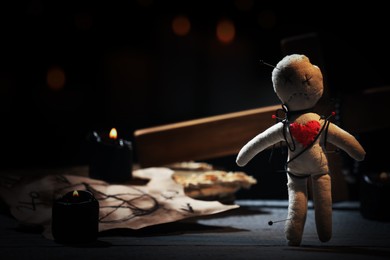 Voodoo doll pierced with pins and ceremonial items on wooden table in darkness