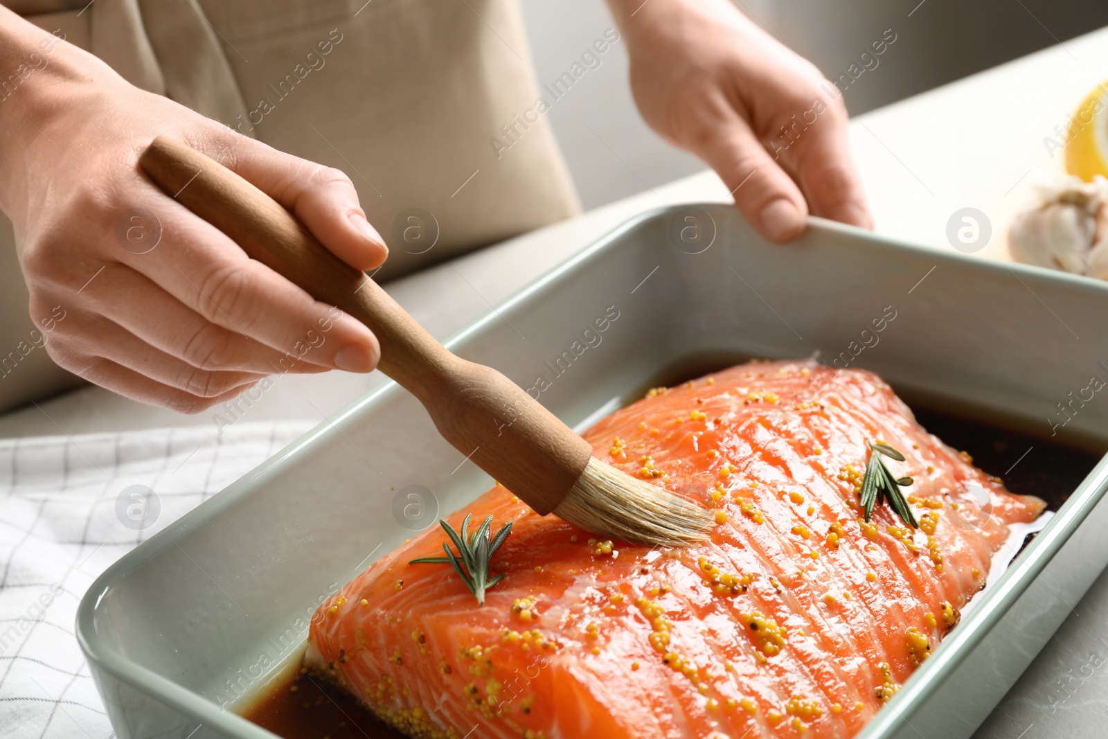 Photo of Woman marinating raw salmon in dish at table