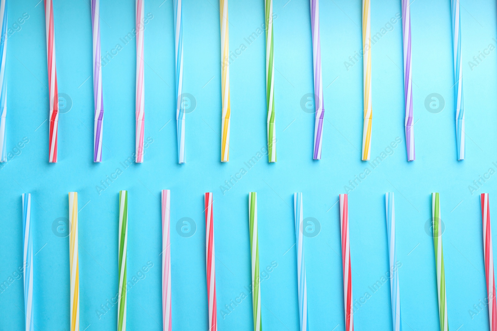 Photo of Colorful plastic drinking straws on light blue background, flat lay