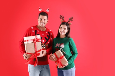 Beautiful happy couple in Christmas headbands and sweaters holding gifts on red background