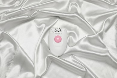 Photo of Modern epilator on white silk fabric, top view. Hair removal