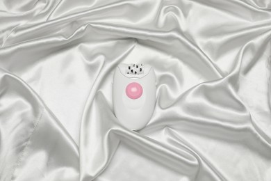 Modern epilator on white silk fabric, top view. Hair removal